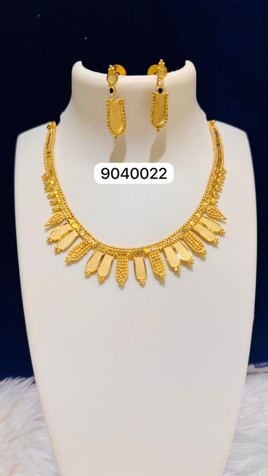 Gold necklace and earrings set on a white stand with a dark background