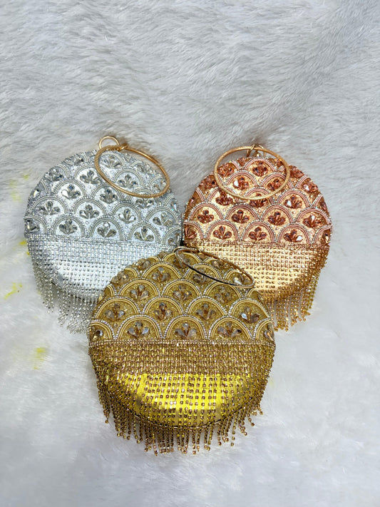 Three decorative handbags in gold, silver, and rose gold on a textured white background.