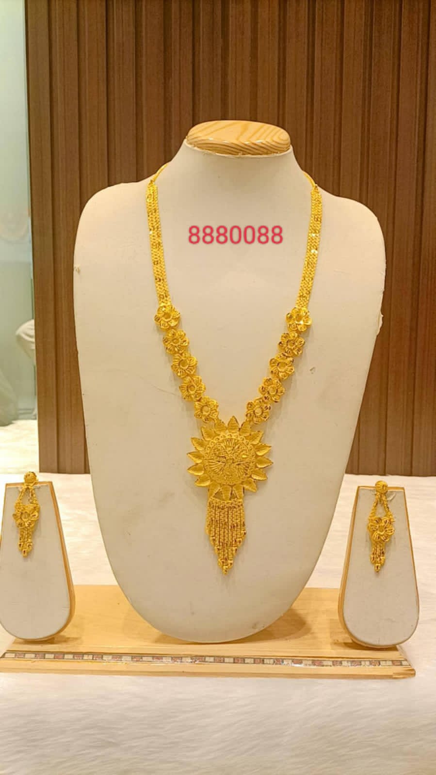 A mannequin showcasing a gold-plated necklace with earrings and ring, with a decorative pattern.